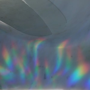 Pu&ograve; includere: Primo piano di una superficie olografica con colori arcobaleno iridescenti che si riflettono su di essa.