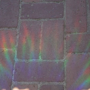 K&ouml;nnte beinhalten: Nahaufnahme einer Backstein-Terrasse mit Regenbogen-Lichteffekt. Die rotbraunen Ziegelsteine werden von einem Regenbogen aus Farben beleuchtet, wodurch eine lebendige und farbenfrohe Darstellung entsteht.