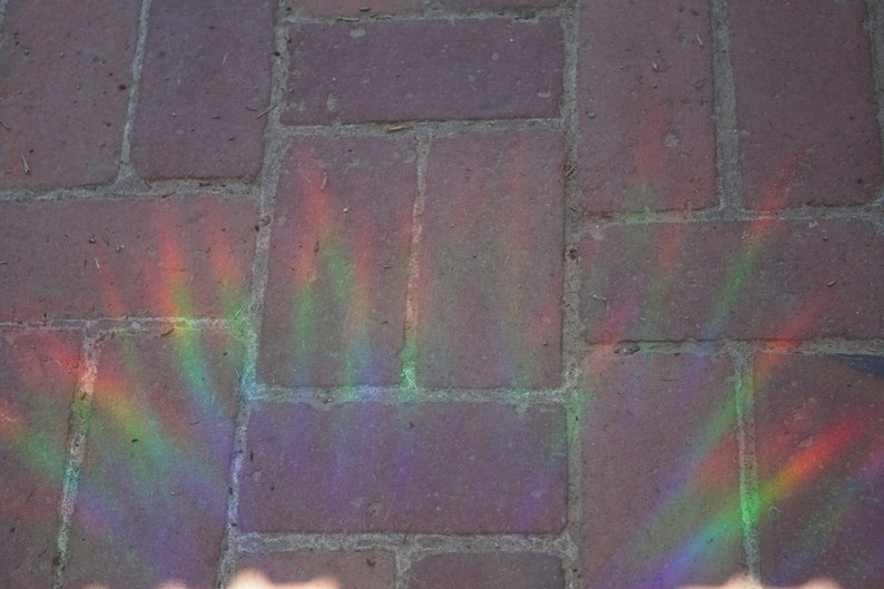 K&ouml;nnte beinhalten: Nahaufnahme einer Backstein-Terrasse mit Regenbogen-Lichteffekt. Die rotbraunen Ziegelsteine werden von einem Regenbogen aus Farben beleuchtet, wodurch eine lebendige und farbenfrohe Darstellung entsteht.