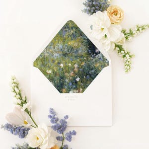 以下が含まれることがあります： 白い封筒の中に花の絵が描かれ、新鮮な花のアレンジメントで囲まれています。花には白、黄色、紫の花があり、緑の葉があります。封筒は開いており、風景画が描かれています。