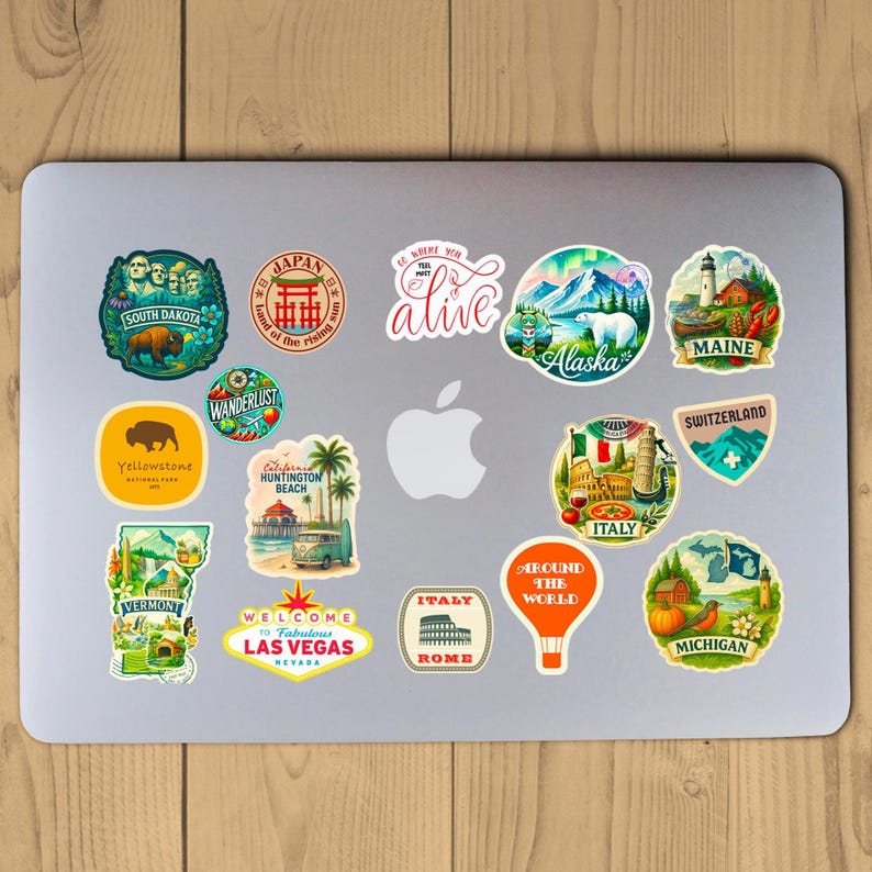 Puede incluir: Una colecci&oacute;n de pegatinas coloridas con tem&aacute;tica de viajes en un port&aacute;til. Las pegatinas presentan destinos como Alaska, Italia y Las Vegas. Los dise&ntilde;os incluyen un oso, un faro, un globo aerost&aacute;tico y texto como "Around the World".