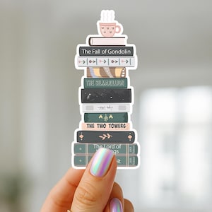 May include: A sticker featuring a stack of books with titles like "The Fall of Gondolin" and "The Silmarillion." A pink teacup with hearts sits atop the stack. The books are in various colors, including black, green, and brown.