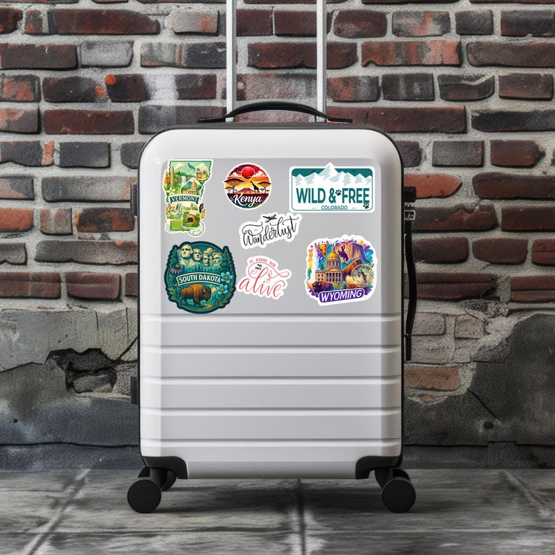 Puede incluir: Una maleta blanca adornada con pegatinas tem&aacute;ticas de viajes. Las pegatinas incluyen im&aacute;genes de paisajes y texto como "Wild & Free Colorado", "Kenya", "South Dakota", "Wyoming" y "Wanderlust". La maleta tiene un asa retr&aacute;ctil y ruedas.