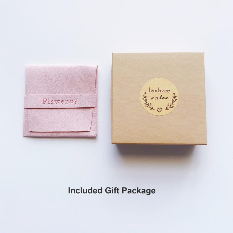 Op de afbeelding: Een lichtroze su&egrave;de etui met het woord "Piswency" in reli&euml;f op de voorkant, naast een kleine, vierkante, lichtbruine geschenkdoos. De doos heeft een ronde sticker met de tekst "handmade with love" met een hart- en bladmotief.