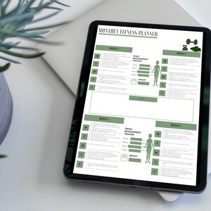 May include: A digital tablet displaying a monthly fitness planner with four weeks of workout schedules. The planner includes a start and finish measurement tracker with a silhouette of a person and a weight scale. The tablet is on a white surface with a green plant in a pot.