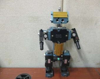 May include: A blue and black robot made of pneumatic cylinders and valves. The robot has a yellow head with a black and white label that says "SMC".