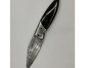 May include: A folding knife with a black handle and a silver blade. The blade has a textured pattern. The knife is open, displaying the full length of the blade. The handle is smooth and curved, with a polished finish. The knife appears to be made of metal.
