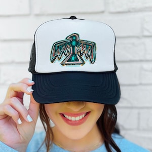 May include: A black and white trucker hat with a colorful Native American-style bird design on the front. The hat has a black mesh back.
