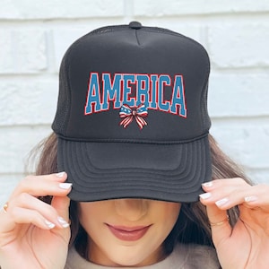 May include: A black trucker hat with a blue and red "AMERICA" graphic and a red, white, and blue bow. The bow has stars on it.