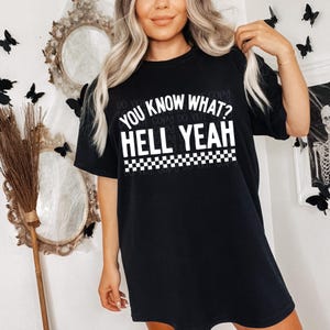 May include: Black oversized t-shirt with white text that reads "You know what? Hell yeah" with a checkered pattern underneath the text.