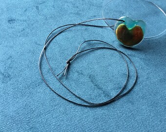 May include: A heart-shaped pendant necklace with a green and gold resin design. The necklace is made with a black cord.