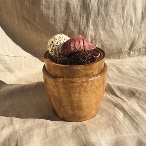 Peut inclure: Un bol en bois avec une finition en bois naturel, contenant un arrangement de fleurs séchées blanches et roses.