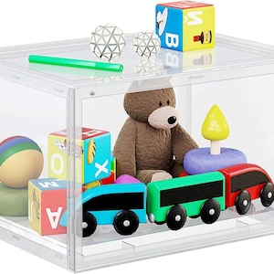 Può includere: Una scatola di contenimento in plastica trasparente con una varietà di giocattoli all'interno, tra cui un orsacchiotto di peluche marrone, un treno, una palla e blocchi. La scatola ha un coperchio ed è realizzata in plastica resistente.