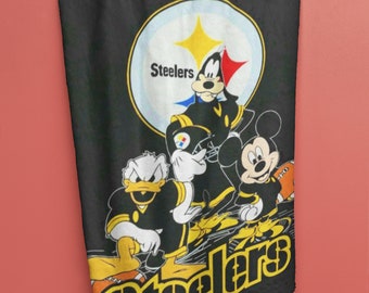 May include: Black fleece blanket with a Pittsburgh Steelers logo and cartoon characters Mickey Mouse, Goofy, and Donald Duck. The logo is yellow and black with the word "Steelers" in yellow.