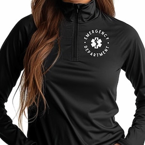 May include: Black long-sleeve athletic shirt with a quarter-zip collar. The shirt features the words "EMERGENCY DEPARTMENT" in a circular design around a white medical symbol on the left chest. The shirt is made of a smooth, possibly moisture-wicking material.