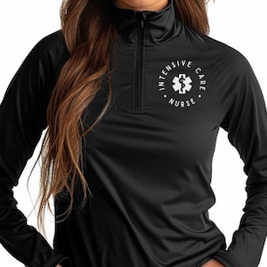 May include: Black long-sleeved athletic top with a quarter-zip collar. The top has a white circular emblem with the words "Intensive Care Nurse" and a medical symbol. The fabric looks like a smooth, performance material.