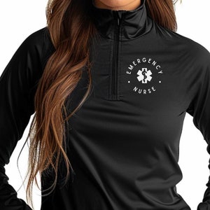Peut inclure: Chemise à manches longues noire avec une fermeture éclair blanche et un logo circulaire blanc qui dit "Emergency Nurse" avec un symbole médical à l'intérieur.