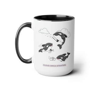 May include: White ceramic coffee mug with a black rim and handle. The mug features a cartoon illustration of three orcas playing musical instruments. The text "CLOUD ORCA-STRATION" is printed on the bottom of the mug.