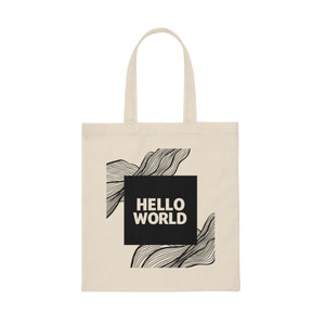 Può includere: Una borsa tote beige con manici neri e un design quadrato nero con il testo "HELLO WORLD" e linee nere astratte.