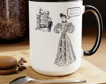 Könnte beinhalten: Weiße Keramiktasse mit schwarzem Rand und Henkel. Die Tasse zeigt eine Schwarzweißillustration einer Frau in einem Kleid, die ein Dokument liest. Das Dokument sagt "SO, IT SAYS HERE...RTFM".
