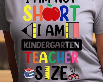 May include: A grey t-shirt with the text "I am not short I am kindergarten teacher size" in colourful letters. The text is surrounded by a red apple, a yellow pencil, a ruler, and a pair of scissors.