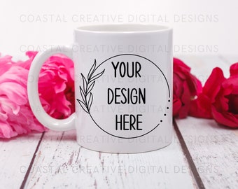 Könnte beinhalten: Eine weiße Keramiktasse mit einem schwarzen Kreisdesign, das einen belaubten Zweig und den Text "YOUR DESIGN HERE" zeigt. Die Tasse steht auf einer weißen Holzoberfläche mit rosa Blumen.