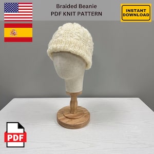 May include: A cream-colored knitted beanie with a braided texture and a ribbed cuff, displayed on a mannequin head. The text Braided Beanie PDF KNIT PATTERN and INSTANT DOWNLOAD are visible, along with the flags of the United States and Spain.