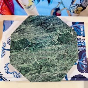 May include: A green octagonal marble serving tray with a unique veined pattern. The tray is on top of a blue and white patterned fabric.