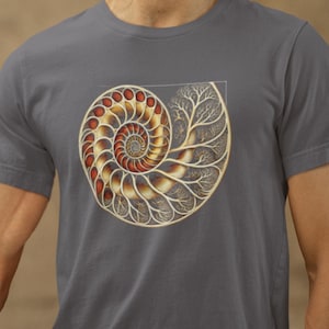 May include: A charcoal gray short-sleeve t-shirt featuring a large, detailed graphic of a nautilus shell. The shell design incorporates warm orange and gold tones with intricate, branching, tree-like patterns integrated into the spiral structure.
