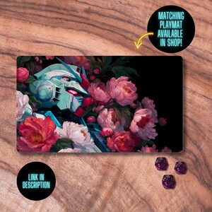 K&ouml;nnte beinhalten: Spielmatte mit einem t&uuml;rkis-roten Roboterkopf, umgeben von rosa und wei&szlig;en Pfingstrosen auf schwarzem Hintergrund. Die Spielmatte tr&auml;gt die Texte "Matching Playmat Available in Shop!" und "Link in Description" in schwarzen Kreisen. Drei lila W&uuml;rfel sind sichtbar.