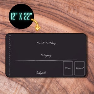 May include: Black gaming mat with white text and lines. The mat is 12 inches by 22 inches and has sections for cards in play, drying, inkwell, draw, and discard.