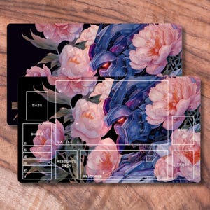 May include: Two black playmats with a floral and robot design. The mats feature a blue robot head with red eyes, surrounded by pink peonies. The mats have labeled areas for gameplay, including "BASE", "SHIELD", and "DECK".