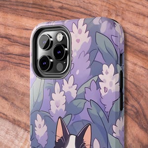 May include: A purple and green phone case with a white cat and a floral pattern. The case has a camera cutout and a black border.