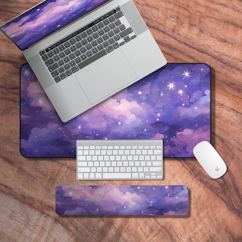 May include: A purple and pink starry sky themed desk mat with a matching wrist rest and keyboard. The desk mat has a white wireless keyboard and a white wireless mouse on it.