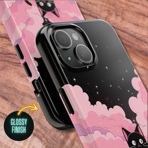 May include: A black phone case with a pink and black design featuring clouds and a black cat. The case has a glossy finish.