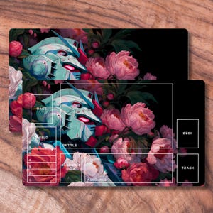 May include: Two rectangular playmats featuring a teal robot head design amidst pink peonies and greenery. The mats have labeled zones for gameplay, including "Deck" and "Trash". The background is black.