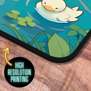 May include: A mousepad featuring a cartoon duck swimming in a blue pond with green lily pads. The mousepad has a black stitched edge.