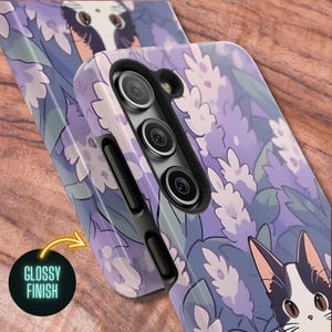 May include: A purple and white floral phone case with a black and white cat illustration. The case has a glossy finish and a camera cutout for a triple lens camera.