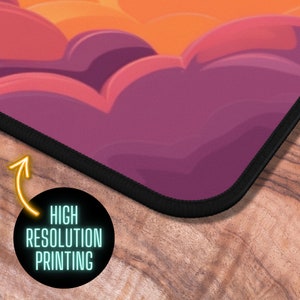 Puede incluir: Un rat&oacute;n de ordenador con tem&aacute;tica de nubes de color rosa y naranja con un borde cosido negro. El rat&oacute;n tiene una impresi&oacute;n de alta resoluci&oacute;n.