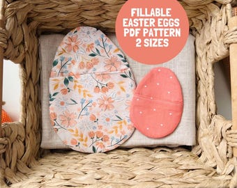 Könnte beinhalten: Zwei eiförmige Stoffbeutel auf einem hellbeigen Tuch in einem geflochtenen Korb. Ein Beutel hat ein Blumenmuster in Pfirsich-, Blau- und Grüntönen, während der kleinere Beutel einfarbig korallenrot mit weißen Punkten ist. Text: FILLABLE EASTER EGGS PDF PATTERN 2 SIZES.