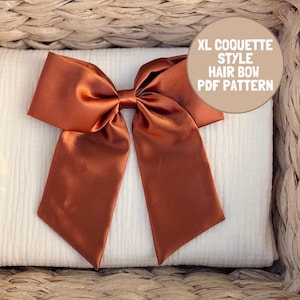 Peut inclure: Un grand nœud pour cheveux en satin de couleur rouille avec de longs pans tombants. Un encart graphique beige circulaire dans le coin supérieur droit contient le texte blanc : XL COQUETTE STYLE HAIR BOW PDF PATTERN. Le nœud est centré.