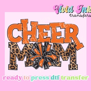 Op de afbeelding: Een DTF-transferontwerp met de woorden "CHEER MOM" in oranje en luipaardprint. Een zwart-oranje pompon staat in het midden. De woorden "Vivid Ink transfers" en "ready to press DTF transfer" staan ook in de afbeelding.