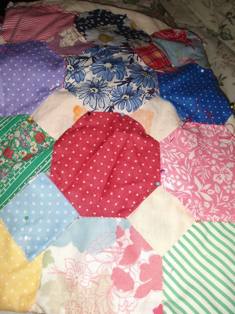 Pu&ograve; includere: Una trapunta patchwork in corso, con una variet&agrave; di motivi floreali e geometrici in tonalit&agrave; di rosso, blu, verde, rosa e giallo. La trapunta &egrave; fissata con spilli di sicurezza e viene cucita a mano.