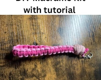 May include: DIY macrame kit with tutorial. A pink and white macrame cord is knotted into a keychain with a silver key ring.
