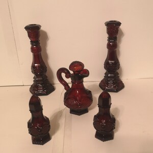 May include: Set of five red glass bottles with a textured design. The set includes two tall candle holders, a jug, and two smaller bottles.