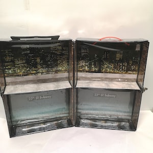 May include: A black and brown cardboard box with a clear plastic window. The box is divided into two sections, each with a cityscape image and the text "23rd ST Subway".