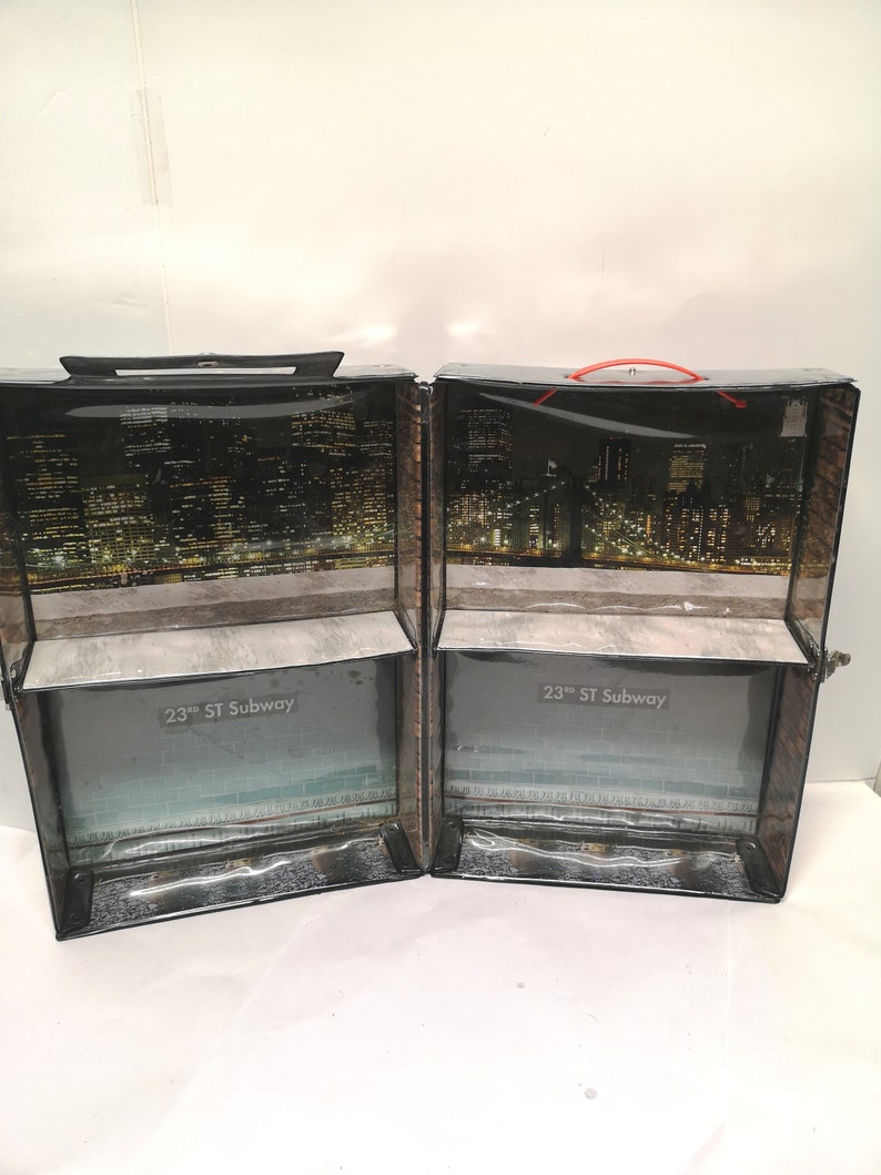 May include: A black and brown cardboard box with a clear plastic window. The box is divided into two sections, each with a cityscape image and the text "23rd ST Subway".