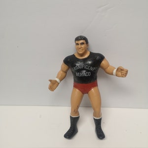 May include: A black and red wrestling action figure with a black shirt that says "Magnificent Muraco".