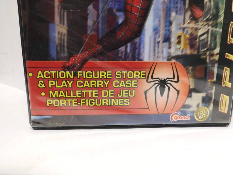 May include: A red and blue Spider-Man action figure store and play carry case with a red and black Spider-Man logo. The text on the case reads "Action Figure Store & Play Carry Case" and "Mallette de Jeu Porte-Figurines".