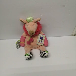May include: Pink plush pig wearing a green hat and zebra print shoes. The pig is holding a sparkly purse and has a tag that says "Manhattan Toy".